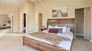 A bedroom with a large bed, a wooden headboard, a bedside table with a lamp, a mirror, and a painting on the wall. - Spacious & Private Home w/ Lazy Mountain View (Palmer)