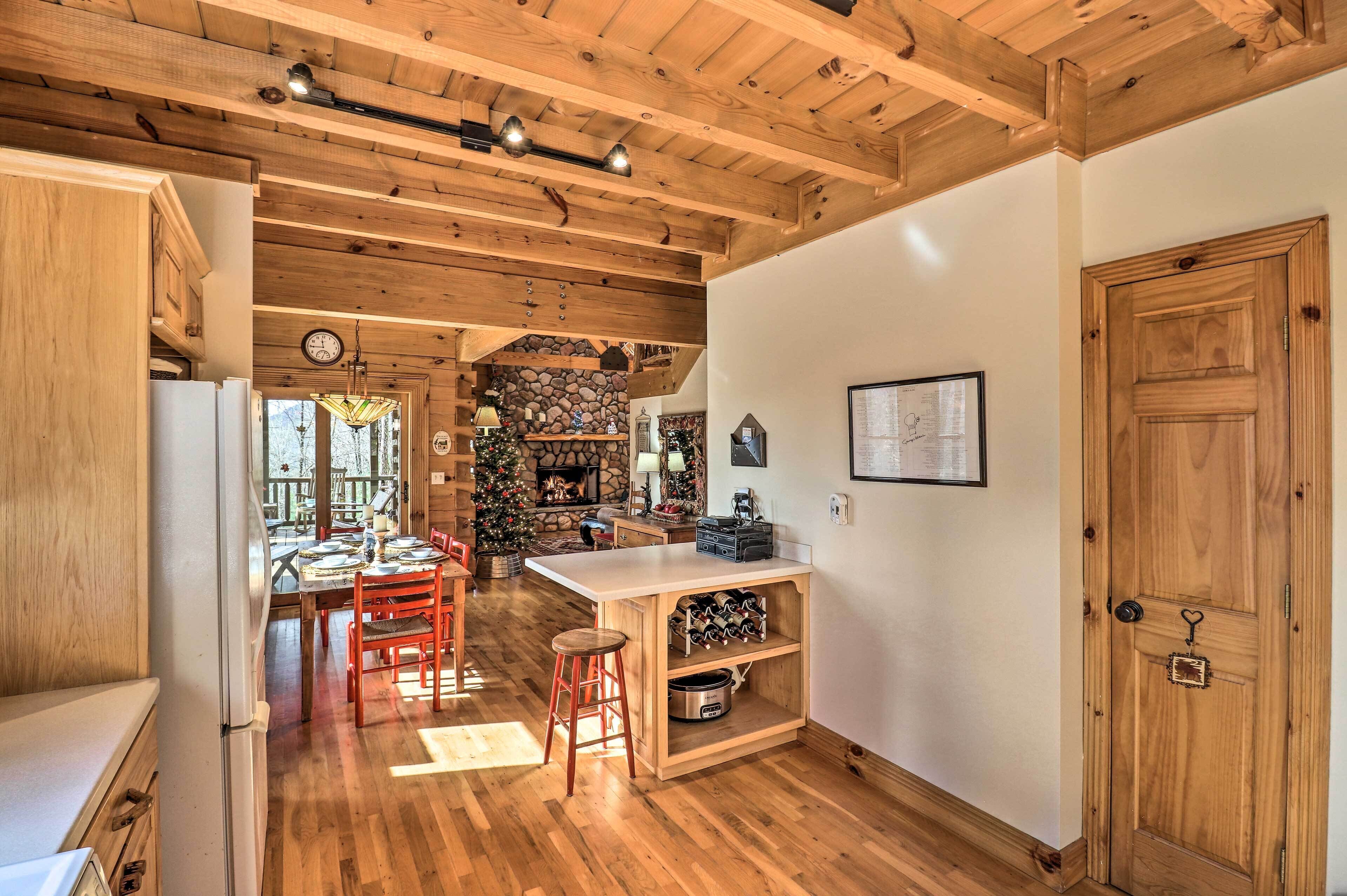 A kitchen with wooden beams, a stone fireplace, and a dining area with red chairs.