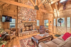 Un interior acogedor de cabaña de troncos con chimenea de piedra, mobiliario de madera y un televisor.