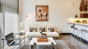 A modern living room with a sofa, a coffee table with a horse sculpture, a side table, a lamp, and a painting of horses.