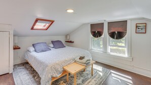 Una camera da letto con un letto, una finestra a soffitto, una panca, una finestra con persiane e un quadro appeso al muro.