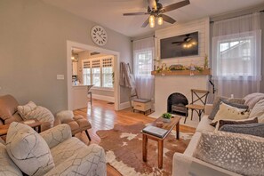A living room with a fireplace, a ceiling fan, and a clock on the wall.