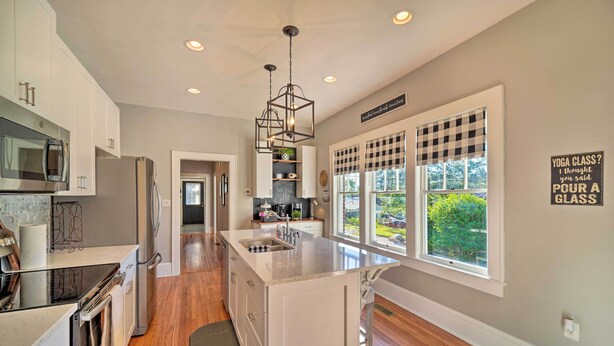 A modern kitchen with white cabinetry, a central island, a built-in microwave, and a large window with a checkered blind.