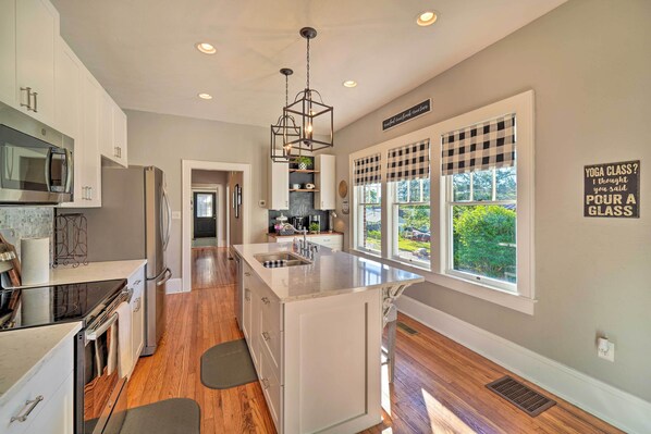 A modern kitchen with white cabinetry, a central island, a built-in microwave, and a large window with a checkered blind.
