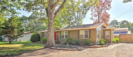 A single-story house with a red door, a front yard with a tree, and a gravel driveway.