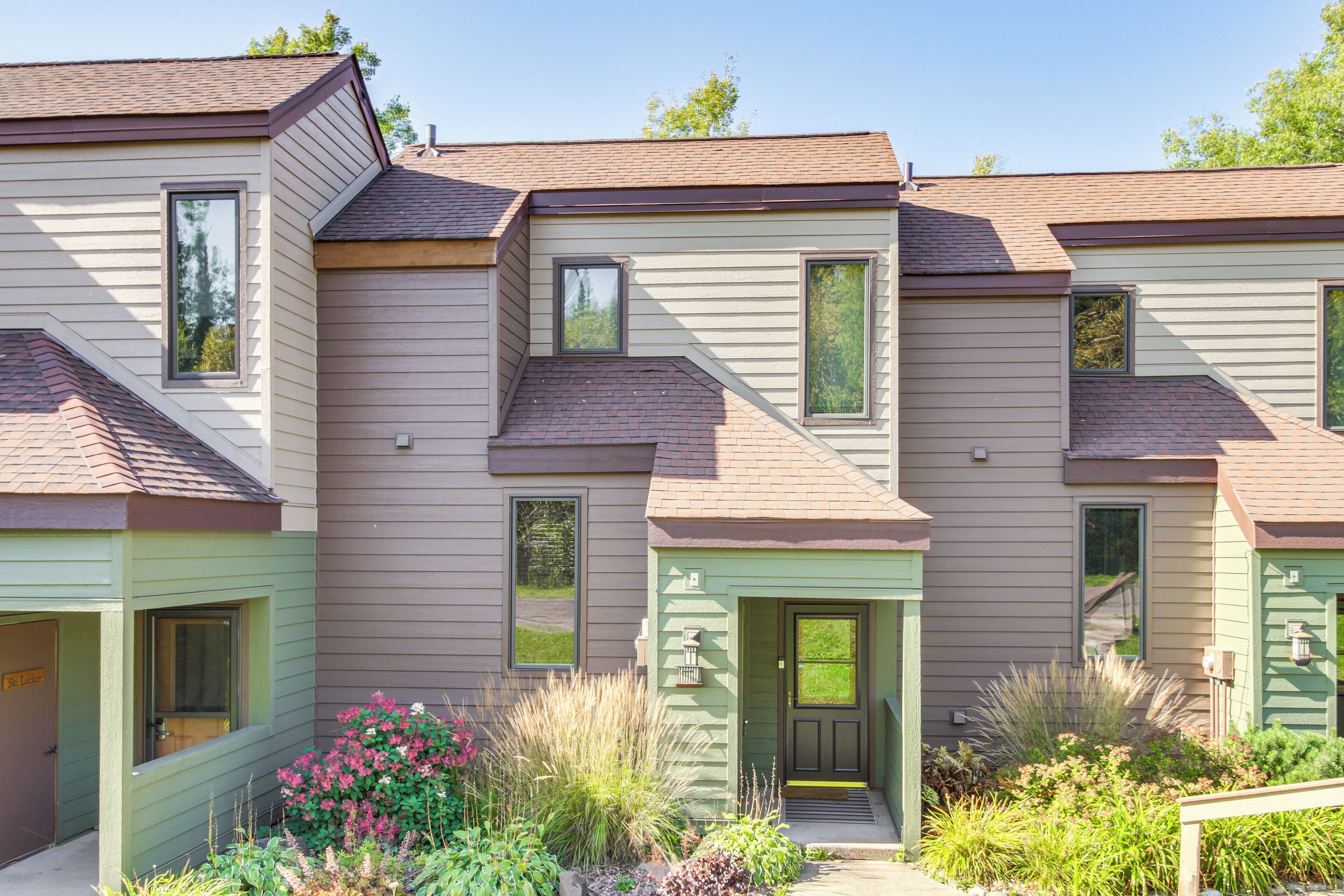 A row of townhouses with a front porch, a small garden with various plants, and a clear sky.