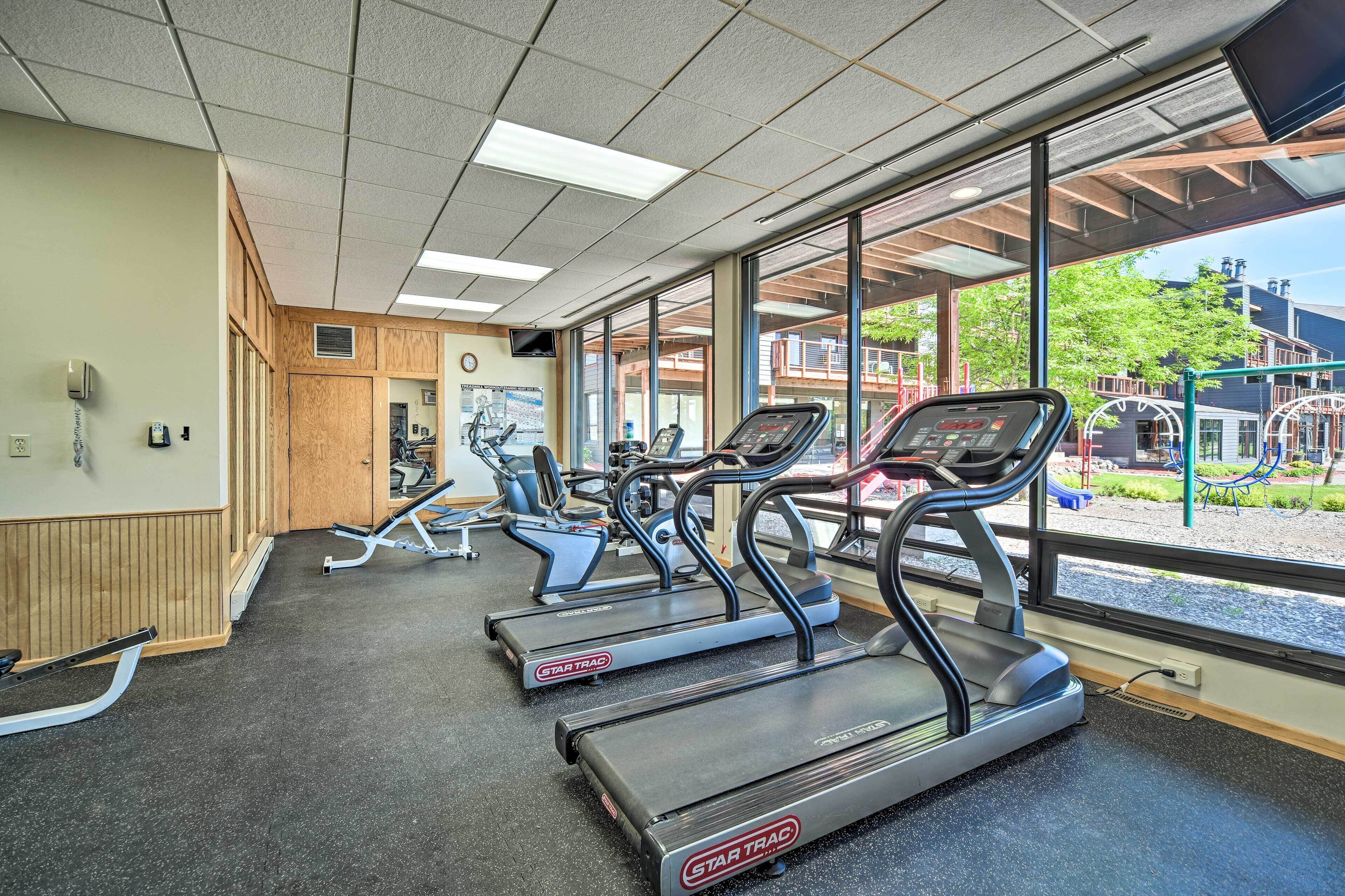 Un gimnasio con cintas de correr, equipo de ejercicio y amplias ventanas con vistas a un espacio exterior.