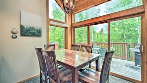 A wooden dining table with chairs, large windows, and a view of a deck and trees. - Lutsen Mountains Retreat w/ Resort Amenities! (Lutsen)
