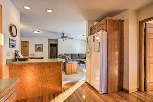 Una cocina con armarios de madera, un refrigerador, un ventilador de techo y una zona de comedor con una mesa y sillas.