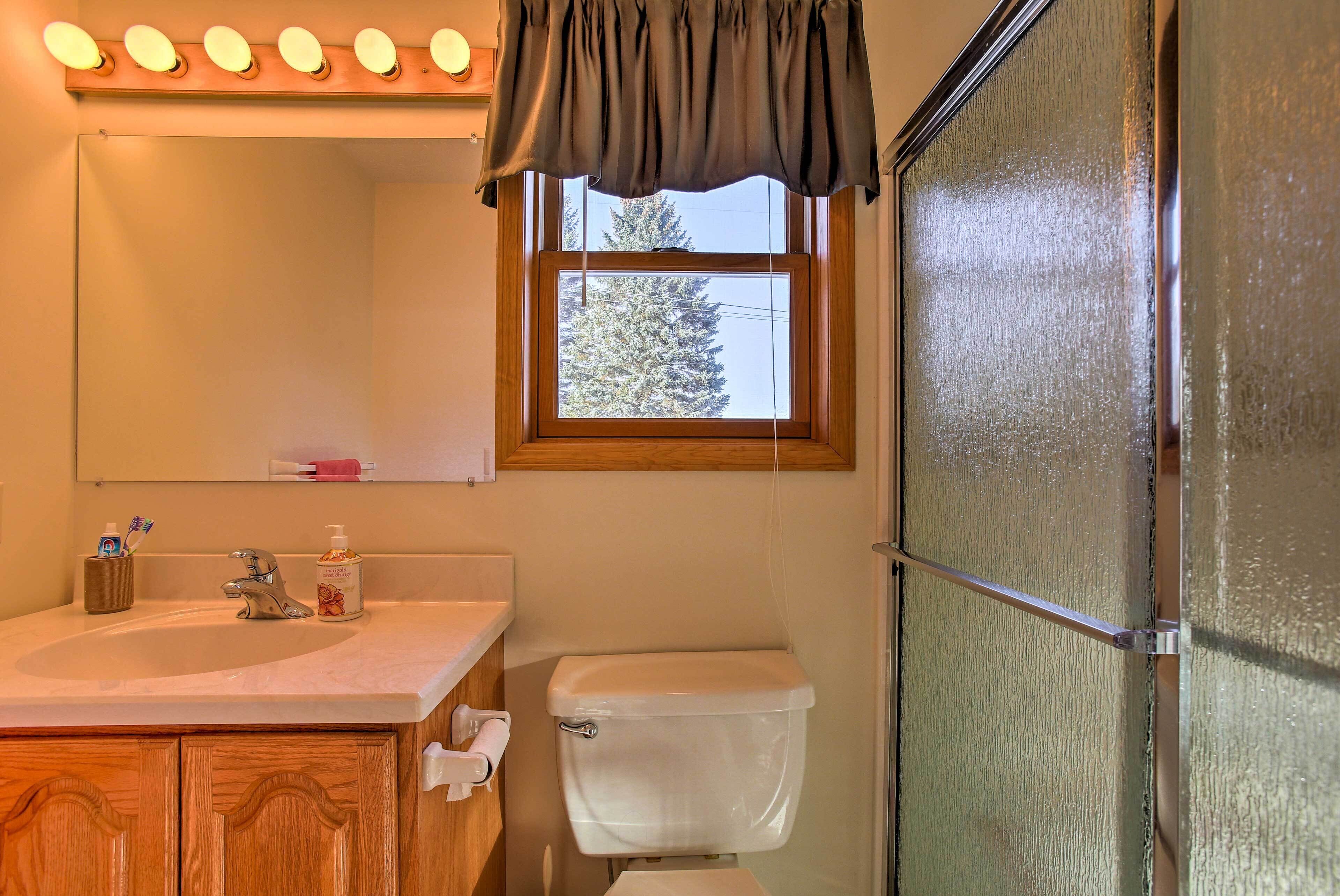 Un baño con lavamanos, espejo, inodoro y ventana con cortinas.