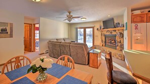 A living room with a sofa, a dining table with chairs, a fireplace, and a ceiling fan.