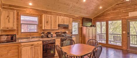 A wooden cabin kitchen with a dining table and chairs, built-in appliances, and large windows.
