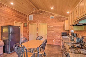 Cocina de cabaña de madera con refrigerador, estufa y mesa de comedor con sillas.