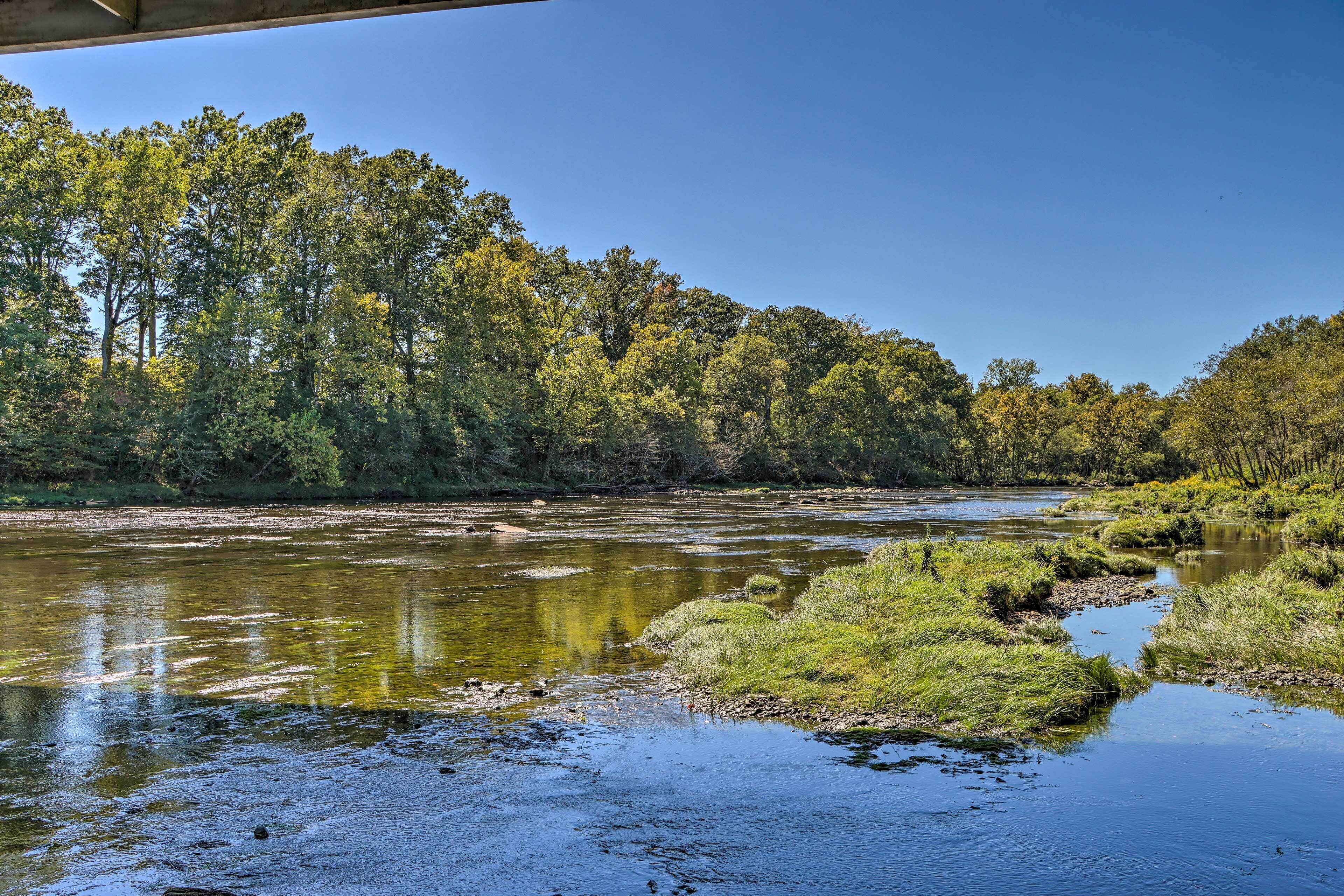 Une rivière bordée de verdure, avec un pont qui la surplombe.