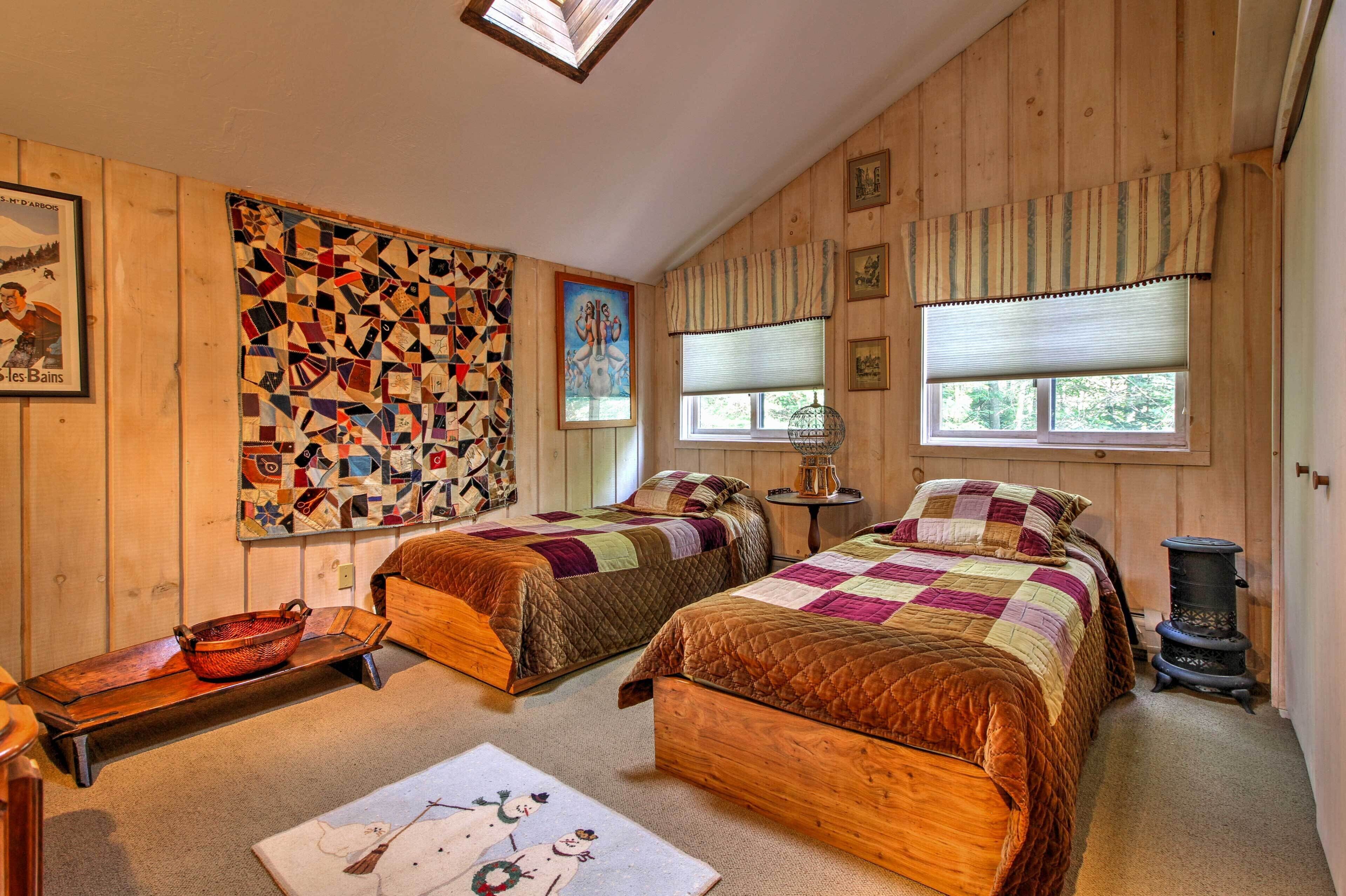 A cozy bedroom with two wooden beds, a quilted wall hanging, and a vintage stove.