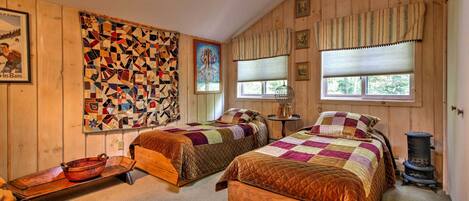 A cozy bedroom with two wooden beds, a quilted wall hanging, and a vintage stove.