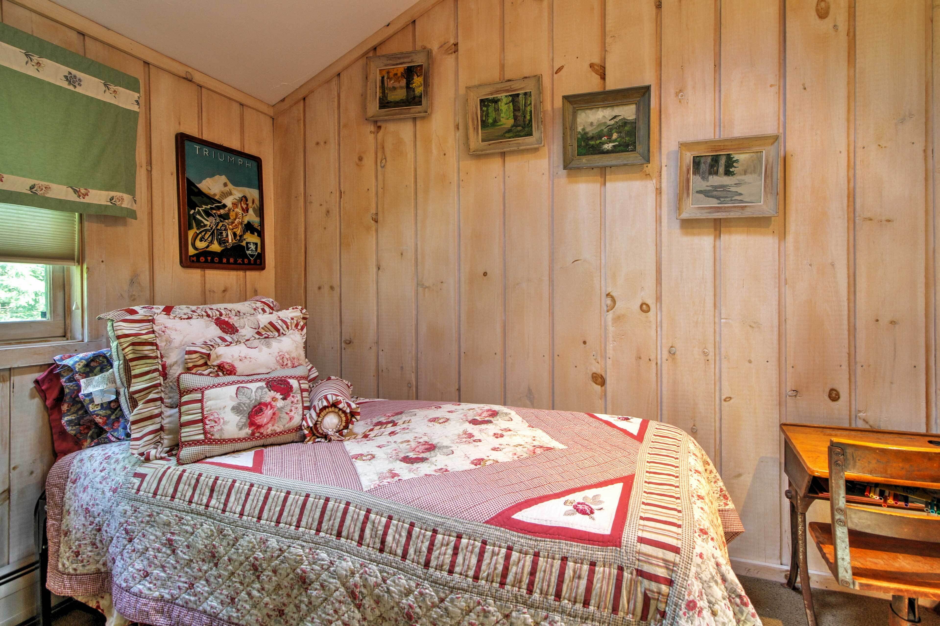 A wooden-paneled room with a bed, a small table, and framed pictures on the wall.