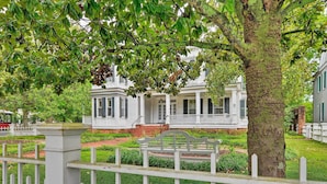 A white colonial-style house with a front porch, surrounded by a well-maintained lawn and a white picket fence.