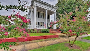 A two-story house with a porch, surrounded by a well-maintained lawn and flowering bushes.