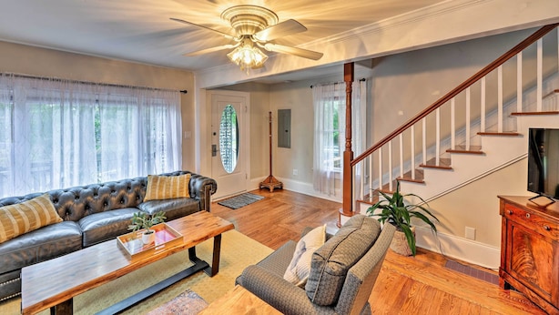 A living room with a leather sofa, a wooden coffee table, a staircase, and a ceiling fan.