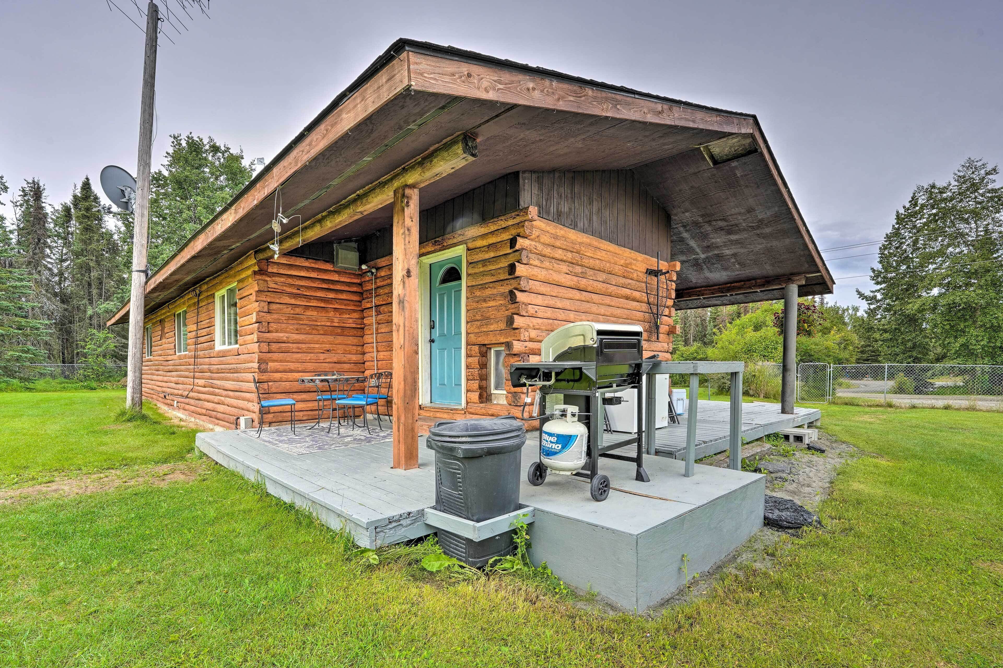 A rustic log cabin with a porch, a grill, and outdoor seating.