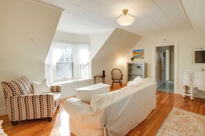 A spacious living room with a high ceiling, a patterned armchair, a covered sofa, and a small table. - Charming Saco Apartment ~ 4 Mi to the Beach! (Saco)