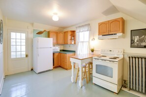 A compact kitchen with wooden cabinets, a white refrigerator, a microwave, a stove, and a window with curtains. - Charming Saco Apartment ~ 4 Mi to the Beach! (Saco)