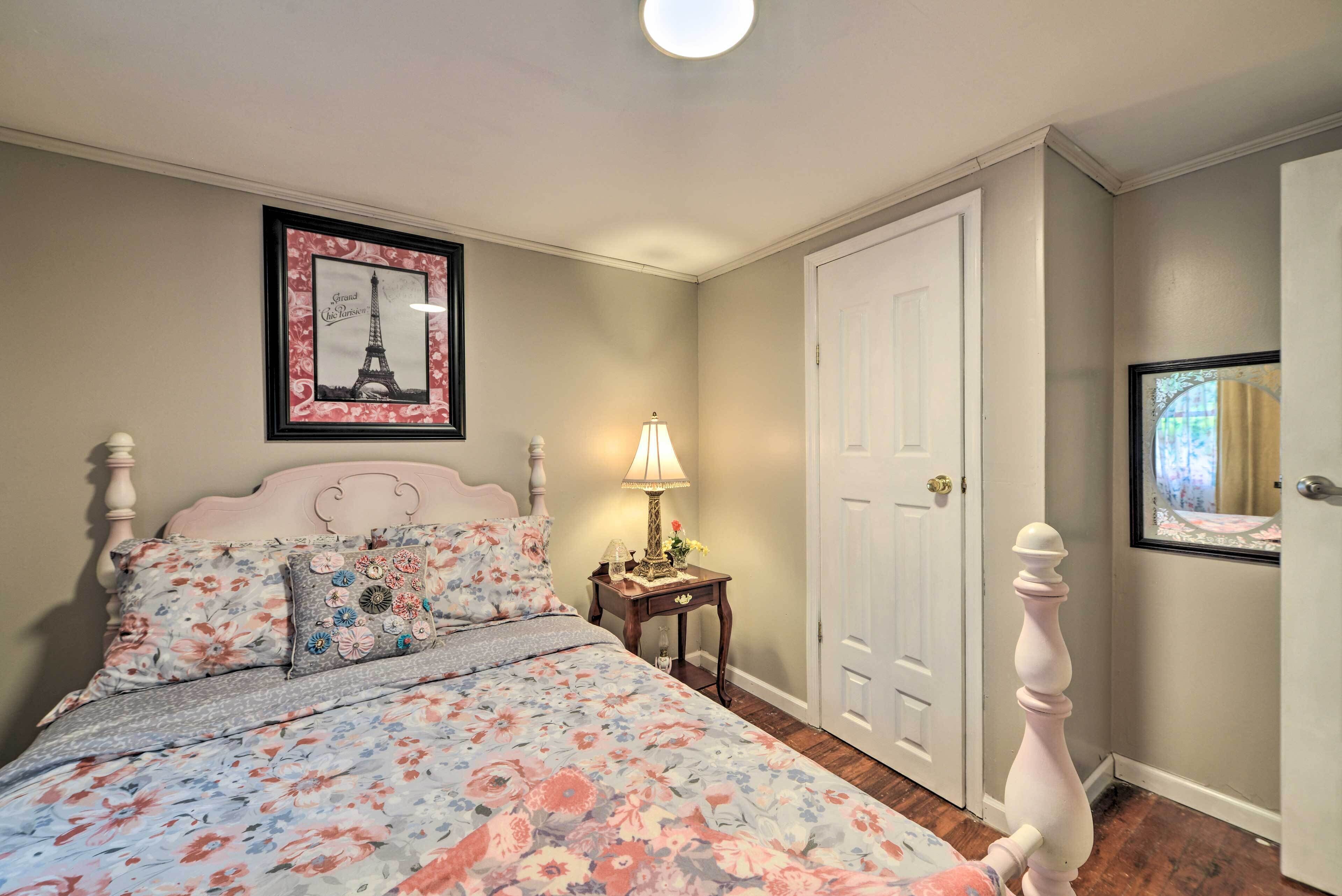 A bedroom with a floral bedspread, a framed picture of the Eiffel Tower, a bedside lamp, and a white door.