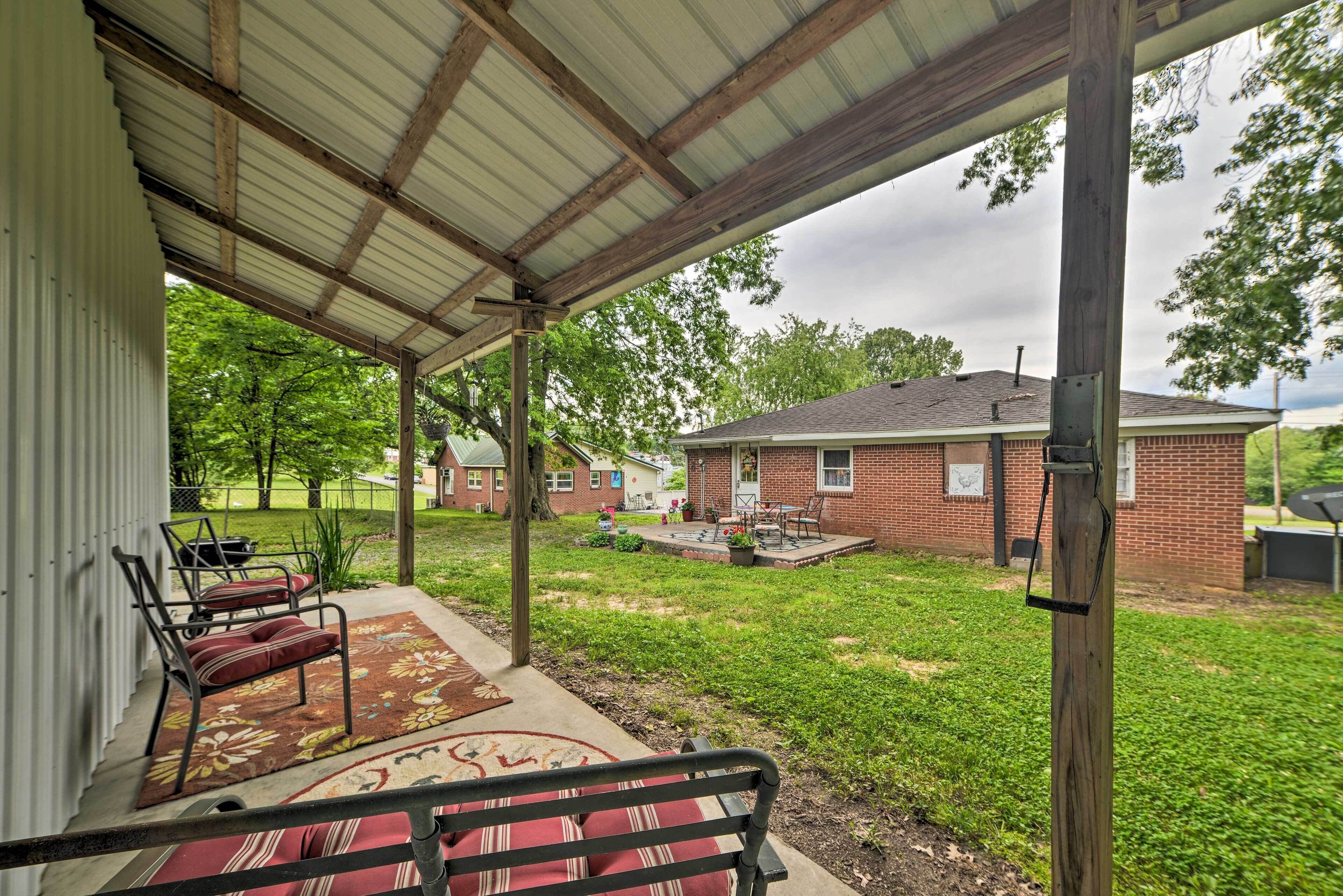 A covered patio with a bench, a rug, and a view of a brick house and lawn.