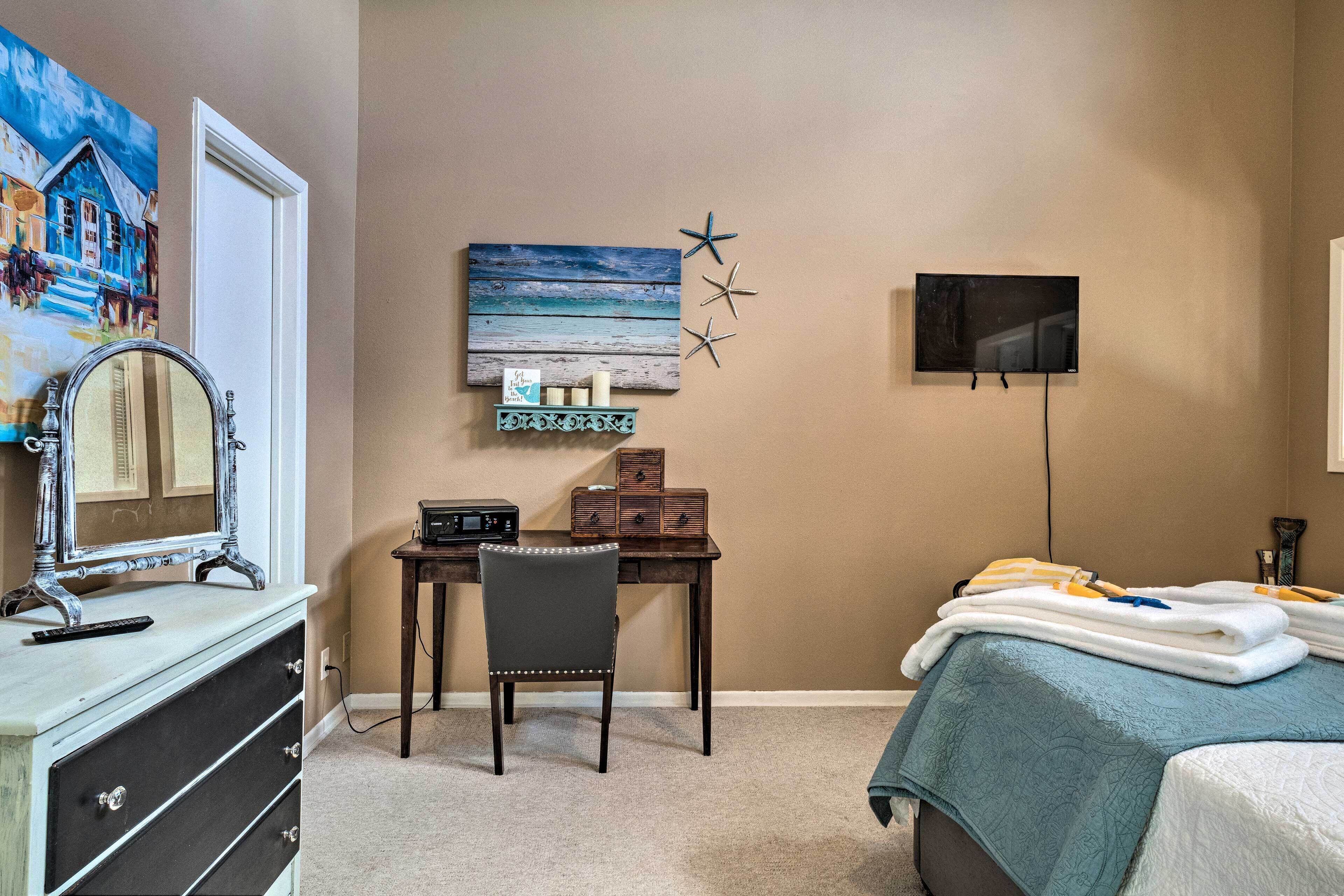 A bedroom with a bed, a desk with a chair, a dresser, a TV, and a wall art piece.