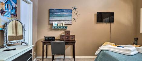 A bedroom with a bed, a desk with a chair, a dresser, a TV, and a wall art piece.