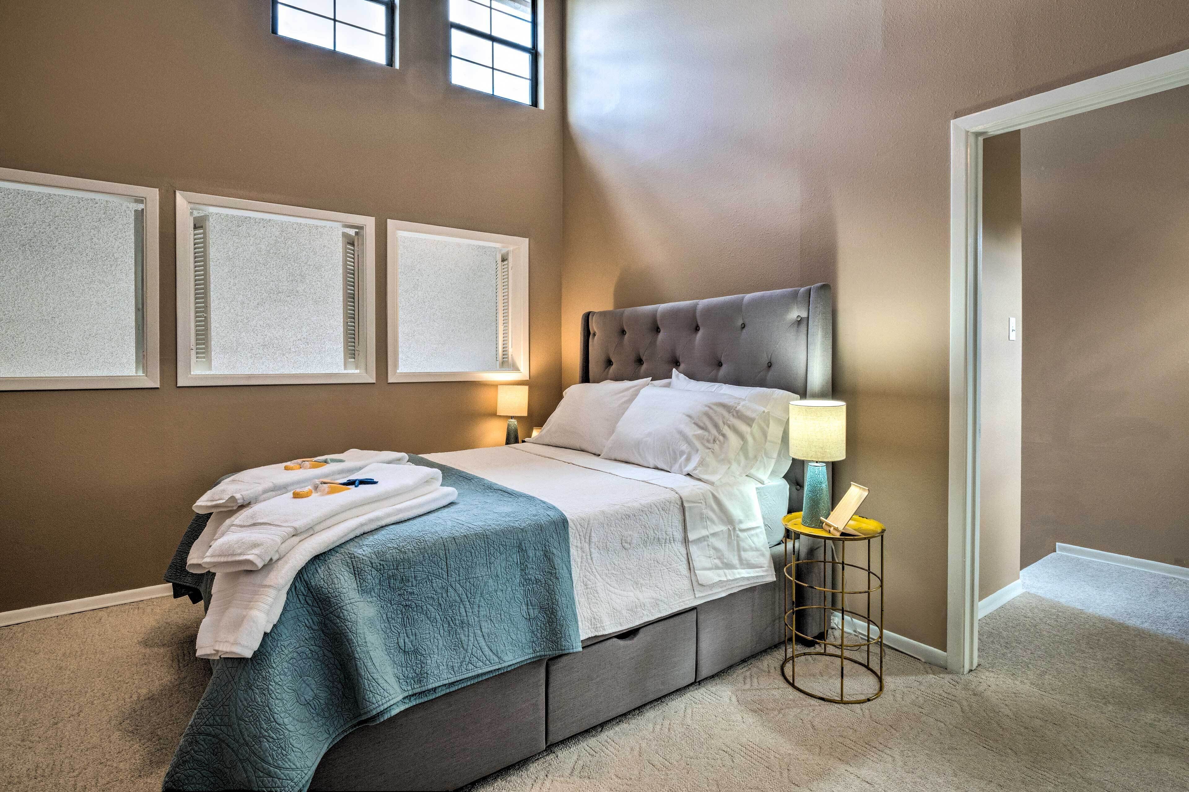 A neatly made bed with white linens and a teal blanket, a bedside lamp, and a small table with a lamp.