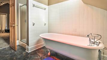 A bathroom with a freestanding bathtub, white tiled walls, and a stone floor.