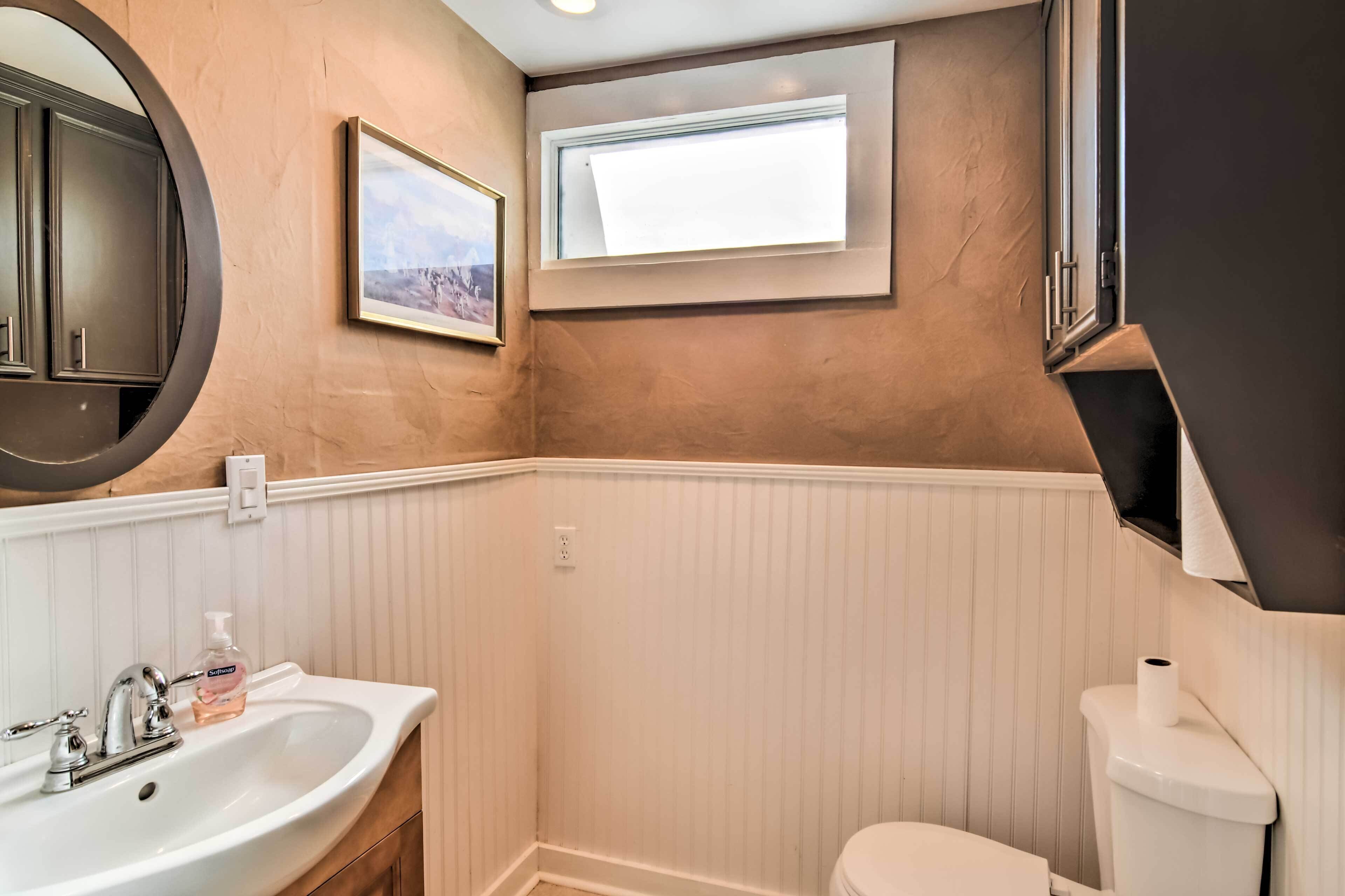 A bathroom with a white sink, a toilet, a window, and a mirror.