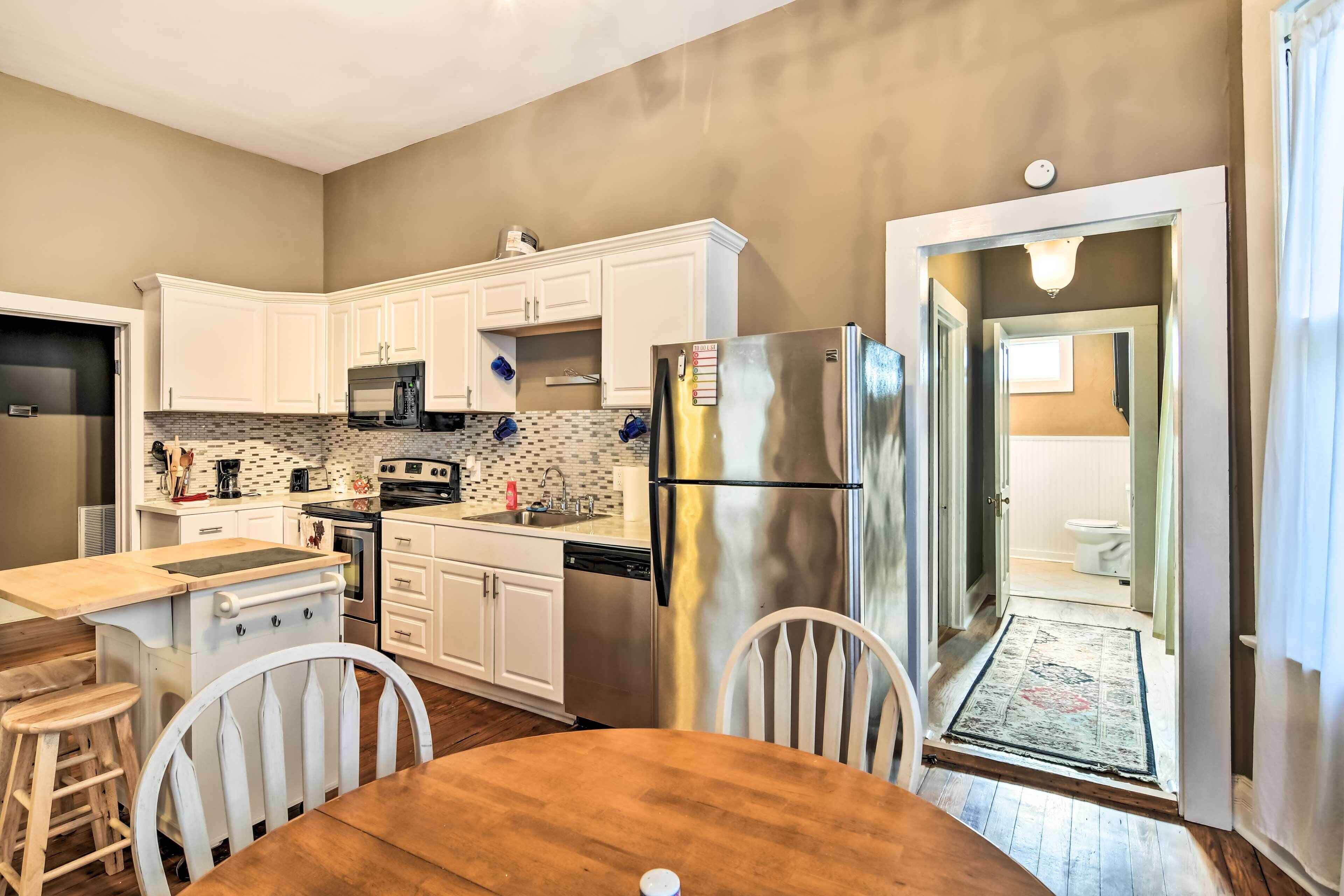 A compact kitchen with white cabinets, stainless steel appliances, and a wooden dining table.