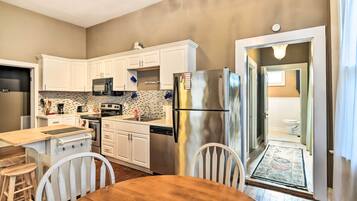 A compact kitchen with white cabinets, stainless steel appliances, and a wooden dining table.