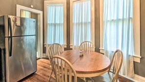 A dining area with a wooden table and chairs, a stainless steel refrigerator, and large windows with sheer curtains. - Stylish Vicksburg Apt w/ Porch - 2 Mi to Casino! (Vicksburg)