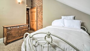 A bedroom with a bed, a wooden dresser, a brick wall, and a door. - Stylish Vicksburg Apt w/ Porch - 2 Mi to Casino! (Vicksburg)