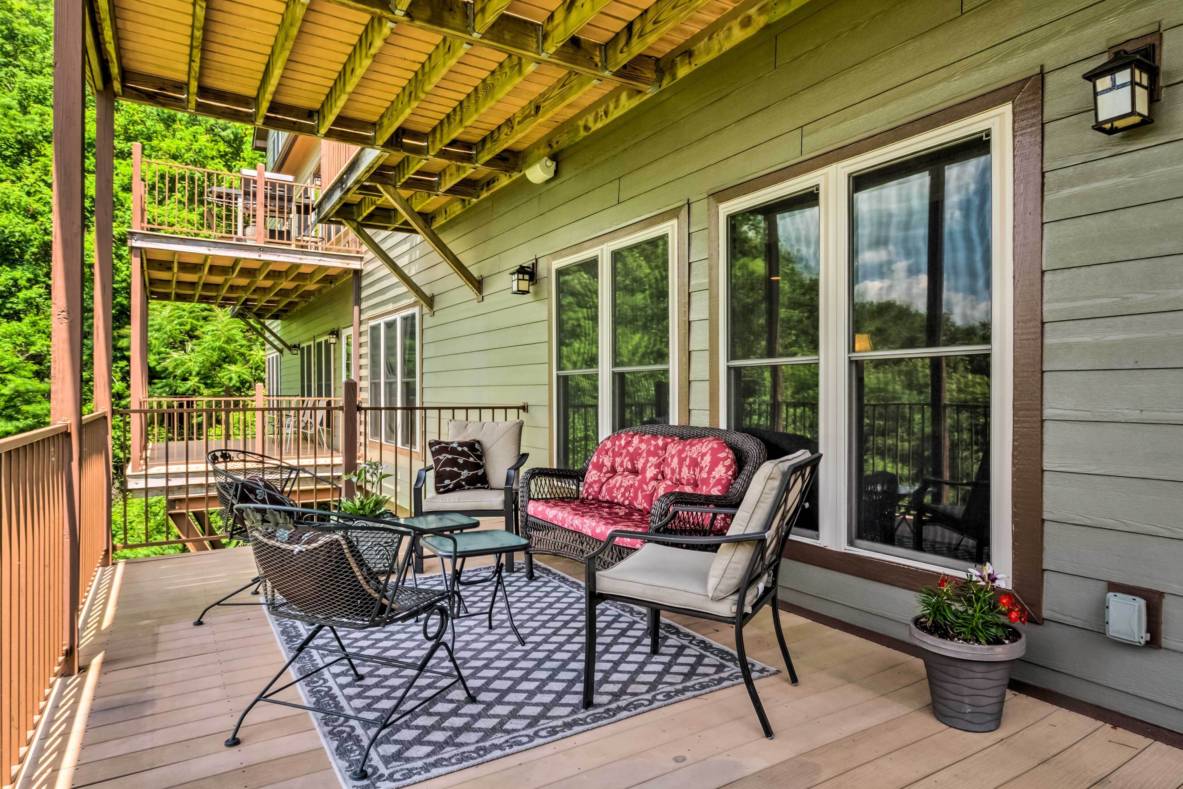 A covered porch with outdoor furniture, a staircase, and large windows.