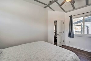 A bedroom with a large bed, a window with curtains, and a door leading to another room.