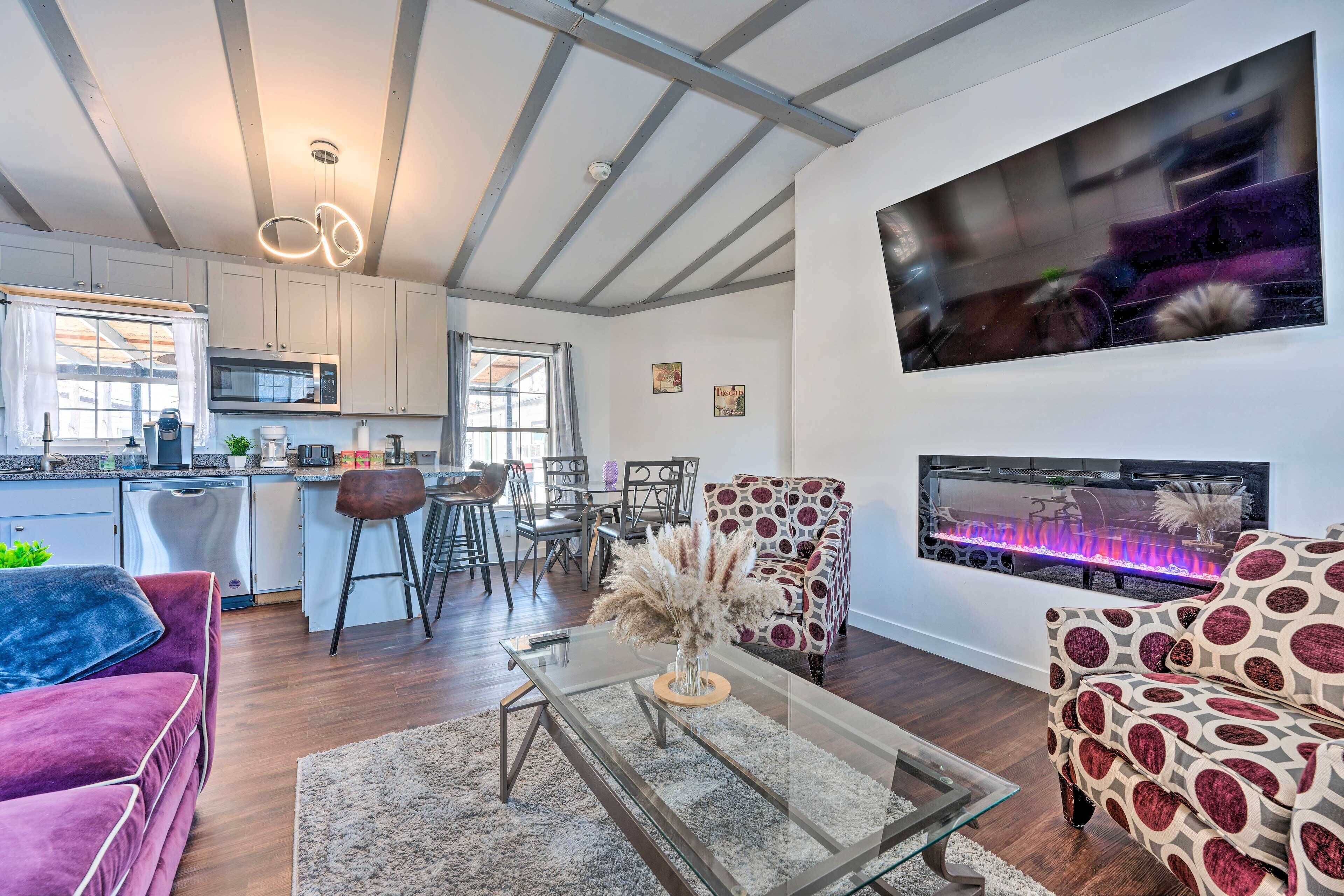 A modern living room with a glass coffee table, a sofa, a patterned armchair, and a fireplace with a TV mounted on the wall.