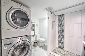 A modern bathroom with a built-in washer and dryer, a shower with a mosaic tile wall, and a toilet.