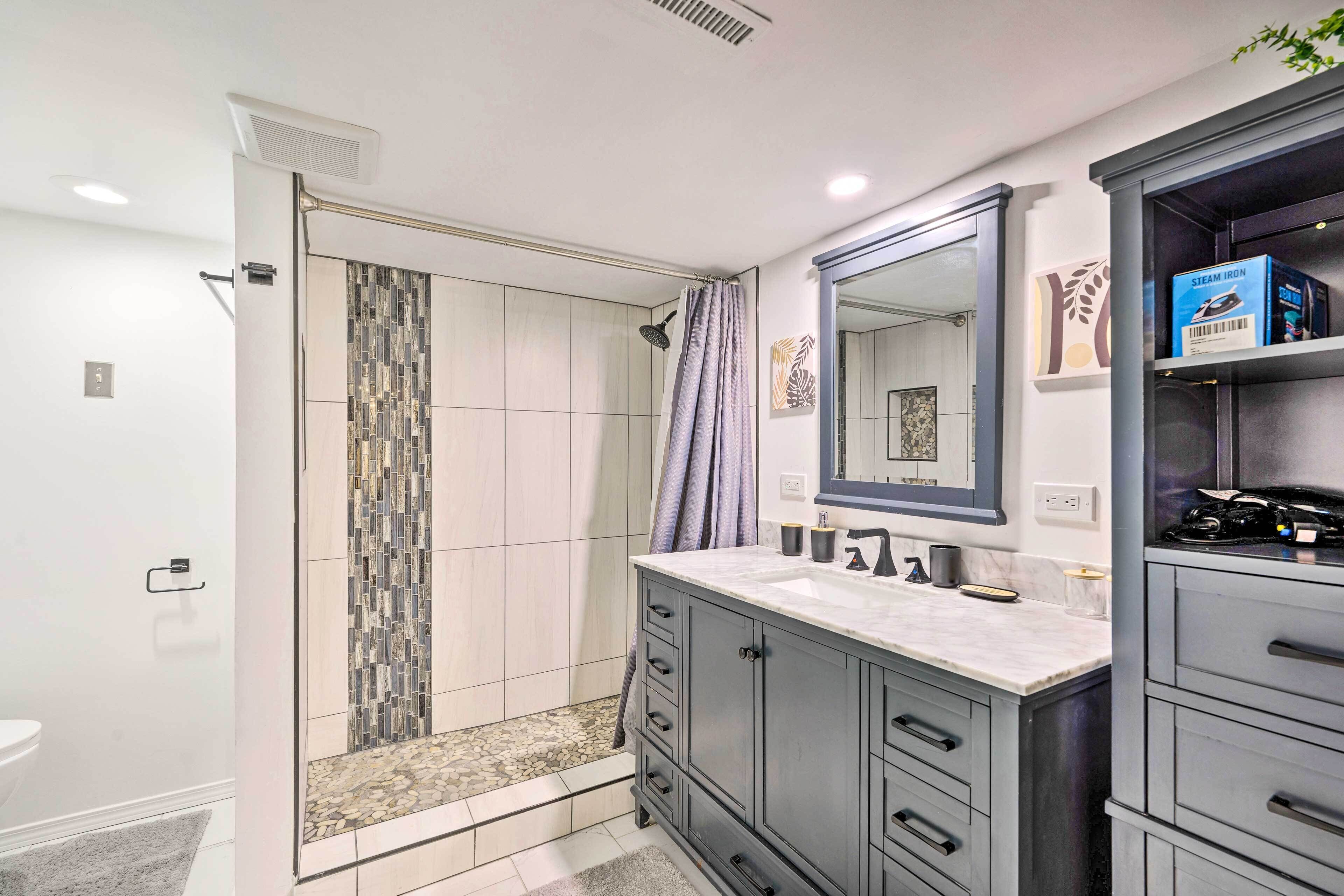 A modern bathroom with a walk-in shower, a large mirror, and a vanity with drawers.