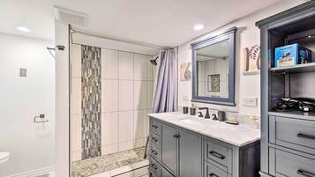 A modern bathroom with a walk-in shower, a large mirror, and a vanity with drawers.