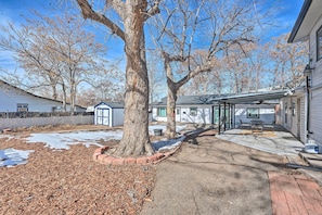 A residential property with a covered patio, a large tree, and a snow-covered ground.