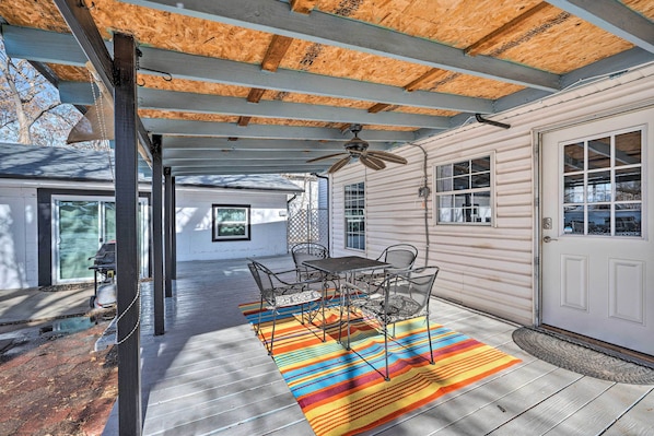 A covered patio with a table and chairs, a ceiling fan, and a colorful rug.