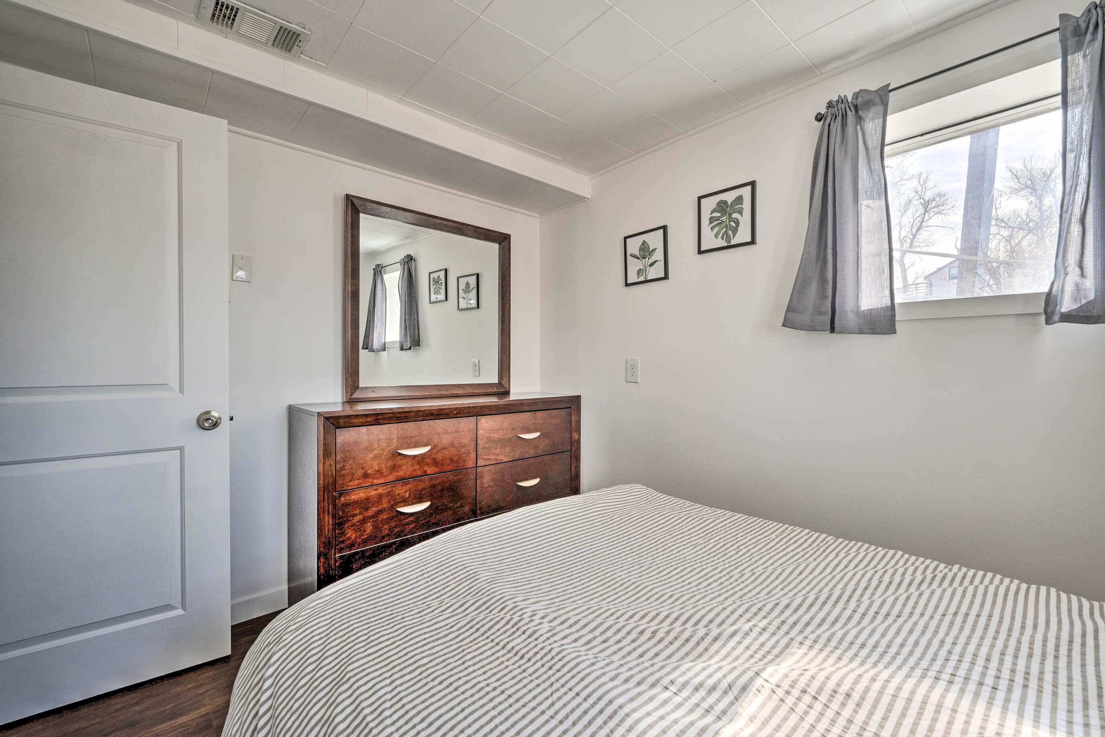 Une chambre à coucher avec un lit, une commode, un miroir et une fenêtre avec des rideaux.