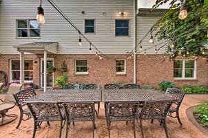 Un patio con una mesa y sillas de metal, luces colgantes y una casa de ladrillo al fondo.