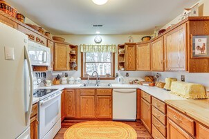 Una cocina con armarios de madera, un refrigerador blanco, un lavavajillas y una ventana con vista a árboles.