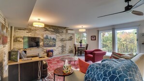 Una sala de estar moderna con una pared de ladrillo, una mesa de centro de vidrio, un sillón rojo y un ventanal con vistas a árboles.